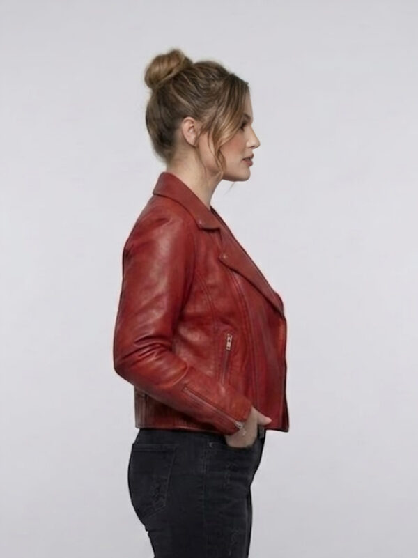 Angled side view of red asymmetrical leather biker jacket with zipper cuffs.